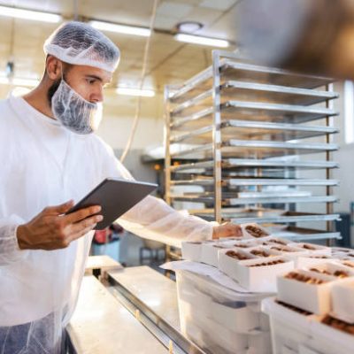 food15 A food inspector in a sterile white uniform is holding the tablet and looking at collected cookies. Food check is important if we want quality and healthy food.